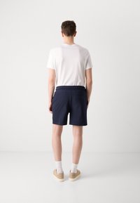 Pantalones cortos azul marino con cintura elástica, bolsillos laterales y un bolsillo trasero, combinados con una camiseta blanca lisa y zapatillas beige.