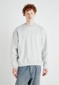 Sweatshirt gris avec un col rond, des manches longues et des poignets côtelés. Le tissu semble doux et texturé, associé à un jean bleu clair.