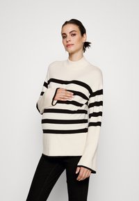Pullover a righe in crema e nero, con colletto alto, maniche ampie e vestibilità relaxed. Tessuto in maglia morbido, con righe orizzontali distintive.