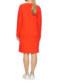 Helles orange-langarm Kleid mit einem strukturierten Chevron-Muster, locker sitzend und mit geradem Saum, kombiniert mit silbernen Plattform-Sneakern.