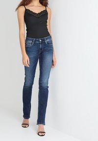 Camiseta de tirantes negra con ribetes de encaje combinada con jeans ajustados azules. El conjunto presenta un diseño ajustado y una textura de denim suave. Sandalias negras de tira.