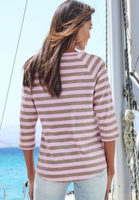 Gestreiftes Langarmhemd in Hellrosa und Braun, mit lockerer Passform, abgerundetem Saum und Raglanärmeln, getragen mit hellblauen Jeans.