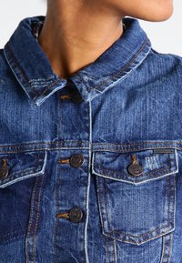 Denimjack met een donkerblauwe kleur, twee voorzakken, zichtbare stiksels en messing knopen. Geweven stof met een klassiek kraagontwerp.