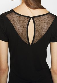 Černé tričko s průhledným síťovaným zadním dílem a vykrojením. Měkká tkanina, krátké rukávy a kulatý výstřih.