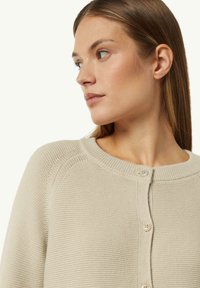 Beige knit cardigan with a round neckline, featuring a button closure and ribbed accents along the collar and placket. Soft texture.