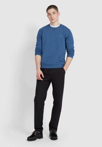 Sweatshirt blu a collo rotondo con polsini e orlo ribattuti, abbinato a pantaloni neri e scarpe nere con lacci marrone chiaro.