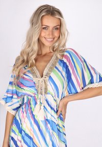 Flerfärgad kaftan med blå, grön och rosa ränder; har spetsdetaljer och ett dekorativt halsringning med fransar. Lättviktsdesign som flödar.