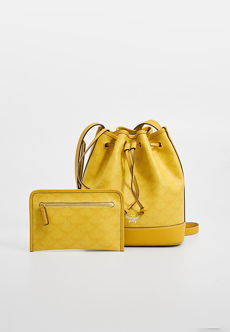 Gelbe Bucket Bag mit strukturiertem Oberflächen und Zugverschluss, begleitet von einem passenden Reißverschlussbeutel. Beide haben goldfarbene Akzente.