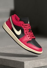 Rdeče in črne usnjene teniske s kremastim srednjim delom, ki imajo zaobljen prst, vezalni obliko in kremasto Nike logotip na strani.