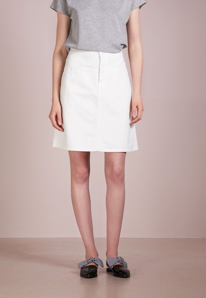White denim skirt with a fitted waist and a straight cut, paired with a gray t-shirt. Black shoes with a gingham bow detail.