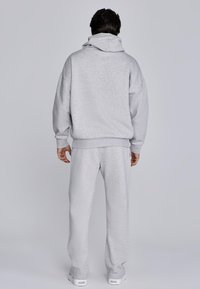 Light gray sweatshirt with hood, loose fit, ribbed cuffs and hem, paired with matching sweatpants, both in soft, textured fabric.