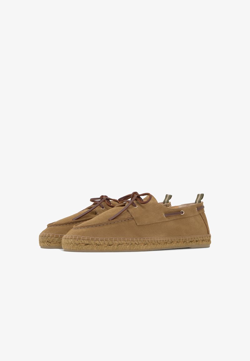 Paire de chaussures style mocassin en daim beige avec des lacets marron et des semelles en corde tressée sur fond blanc.