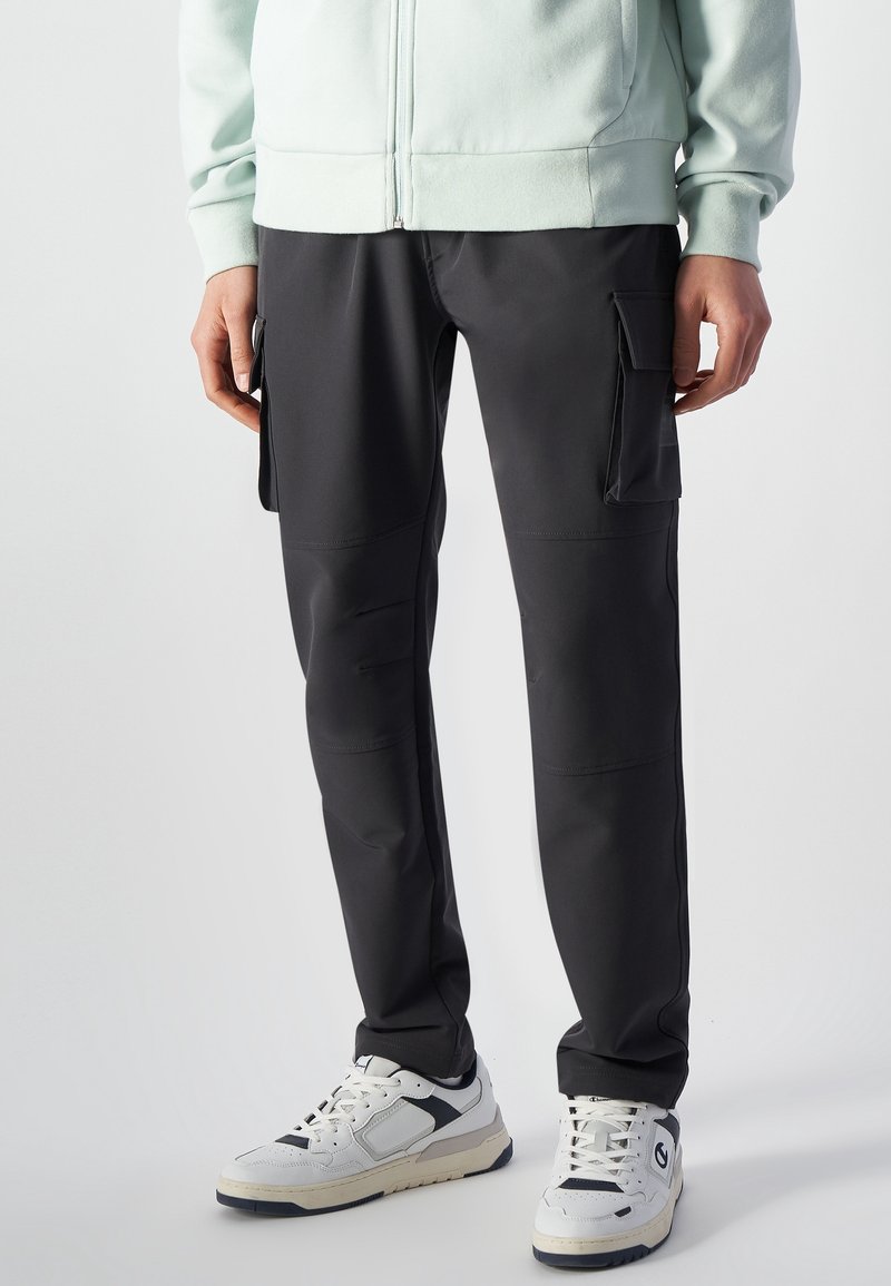 Svarta cargobyxor med flera sidofickor, tillverkade av mjukt, stretchigt material, med en figurnära silhuett. Bärs med vita sneakers.