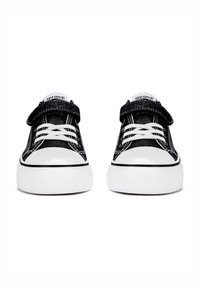 Schwarze Canvas-Sneaker mit weißen Gummisohlen, versehen mit einem strukturierten Obermaterial, weißen Schnürsenkeln, einem Klettverschluss und einem Logo auf der Zunge.