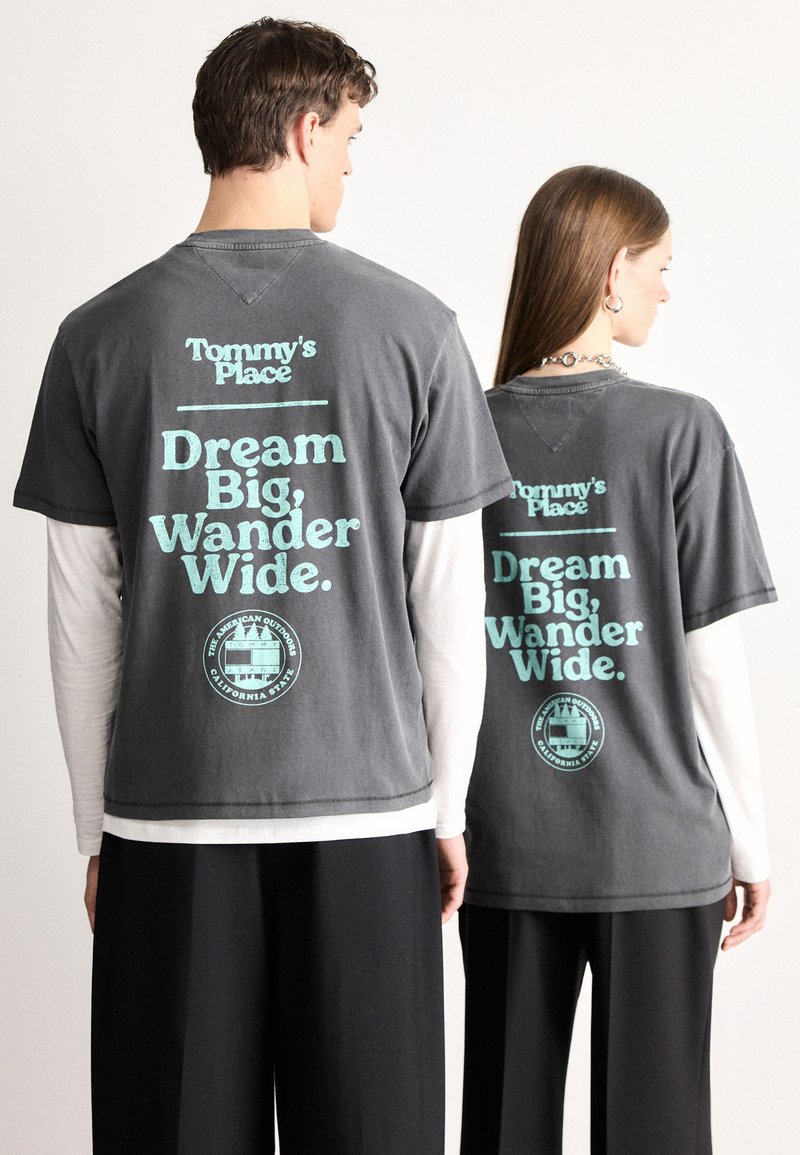 Γκρι βαμβακερά μπλουζάκια με εκτυπωμένο κείμενο σε ανοιχτό μπλε: "Tommy's Place" και "Dream Big, Wander Wide." Καθημερινή, άνετη εφαρμογή με κοντά μανίκια.