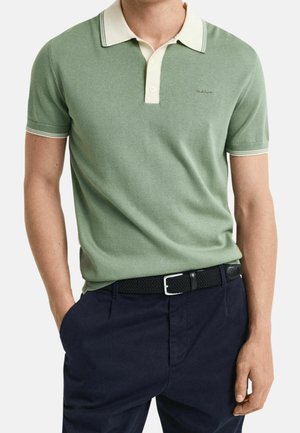 Hellgrünes gestricktes Poloshirt mit weißem Kragen und Knopfleiste; mit navyfarbenen Akzenten an den Bündchen. Kombiniert mit navyfarbenen Hosen und einem schwarzen geflochtenen Gürtel.
