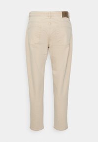 Béžové džíny s rovným střihem nohavic, se dvěma zadními kapsami a hnědou koženou štítkem na pásku. Hladká textura.