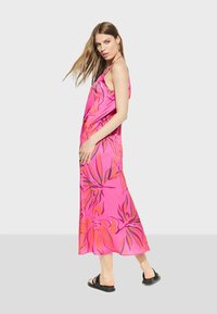 Pink satin maxi dress with large floral patterns in orange and purple, featuring thin straps and a flowy silhouette. Black flat sandals.