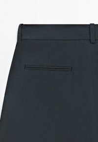 Primo piano di pantaloni da abito grigio scuro che mostrano la vita, i passanti per cintura e una tasca posteriore a filetto singolo.