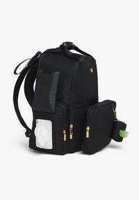 Juodos audinio kuprinės su paminkštintomis petnešomis, keliomis užtrauktukais užsegamomis kišenėmis, šonine skyrele servetėlėms ir mažu nuimamu dėklu su žaliu akcentu.