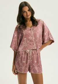 Jasnoróżowy satynowy zestaw do wypoczynku składający się z krótkich rękawów, zapinanej koszuli oraz szortów ze sznurkiem w talii, z białymi akcentami i misternymi złotymi wzorami.