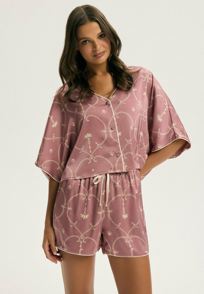 Jasnoróżowy satynowy zestaw do wypoczynku składający się z krótkich rękawów, zapinanej koszuli oraz szortów ze sznurkiem w talii, z białymi akcentami i misternymi złotymi wzorami.