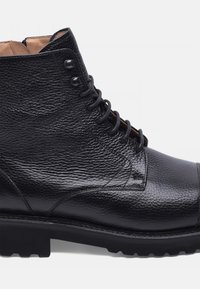 Stivaletto in pelle nera con finitura testurizzata, punta tonda, design con lacci e suola robusta con motivi di trazione per aderenza.