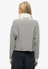 Striped sweatshirt in cream and navy, featuring a folded collar with "Athletic Essentials" embroidered. Cropped design and relaxed fit.