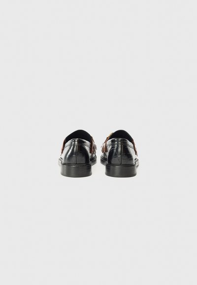 Black shoes with brown leather accents, viewed from the back against a plain white background, showcasing their sleek design and detailing.