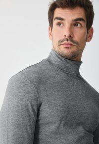 Suéter gris de cuello medio en una suave tela texturizada. Diseño ajustado con mangas largas, sutiles detalles en las costuras y un cuello alto.