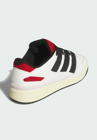White sneaker with black stripes, red mesh accents, and black laces. Features a textured sole and padded collar for comfort.