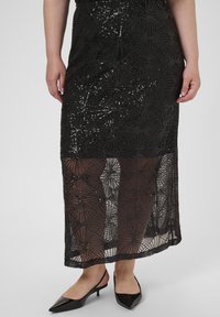 Falda negra adornada con lentejuelas y con un velo transparente, que presenta patrones geométricos. Combinada con zapatos de tacón negro puntiagudos.