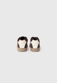 Baskets en daim marron avec un panneau en cuir crème au talon et une semelle en caoutchouc beige. Forme arrondie et design minimaliste.