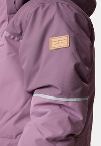 Lila wasserdichte Jacke mit einer Stofftextur, einem Lederlogo-Patch und reflektierenden Details entlang des Ärmels.