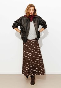 Veste bomber en cuir noir sur une chemise grise, assortie à une jupe maxi à pois marron et des bottines chelsea marron.