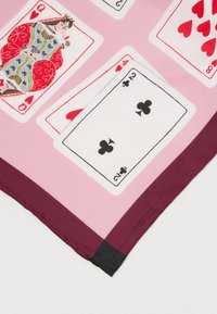 Dizajn hracích kariet zobrazuje kráľovnú srdcových, eso srdcových, dve krížových a osem srdcových na ružovom látkovom podklade s bordovým okrajom.