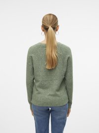 Grønn teksturert strikkegenser med rund hals og lange ermer, kombinert med blå jeans. Bakfra vises ribbestrikkede mansjetter og kant.