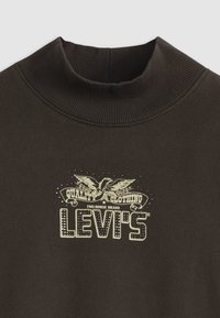 Barna pulóver magas nyakkal, amelyen egy sas és a "Levi's" felirat található arany és fekete díszítéssel. Puha tapintású.
