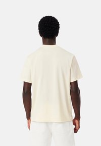 T-shirt a maniche corte, colletto rotondo, in cotone color crema. Presenta una vestibilità comoda con cuciture minime, una texture liscia e senza loghi o motivi visibili.