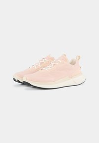 Sneaker atletiche rosa chiaro con superiore in rete traspirante, lacci bianchi e suola in crema imbottita. Presentano una suola in gomma nera per una maggiore aderenza.