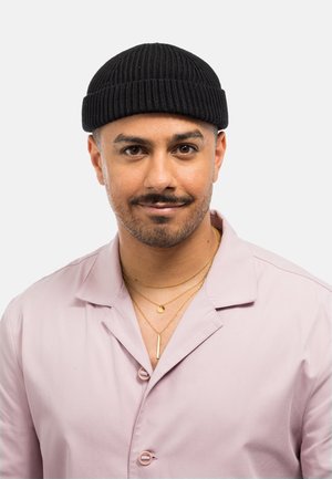Cappello lavorato a maglia nero con una texture a costine; uomo che indossa una camicia button-up rosa pallido e collane d'oro sovrapposte.