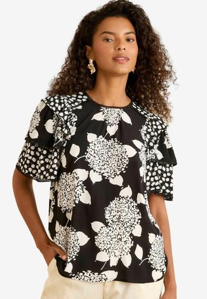 Blusa nera con ampi motivi floreali bianchi, maniche corte a volant con un design a pois e scollatura rotonda con dettagli in pizzo.