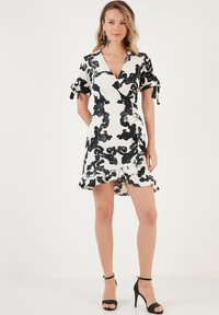 Black and white sequin dress with a V-neck, short tied sleeves, ruffled hemline, and floral pattern. Paired with black high-heeled sandals.
