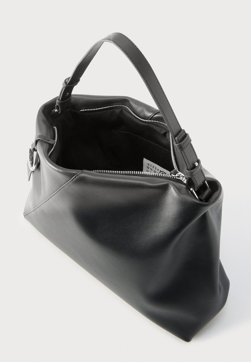 Schwarze Lederhandtasche mit einem einzigen verstellbaren Henkel, einem teilweise geöffneten silbernen Reißverschluss, der ein Stoffetikett im Inneren zeigt.