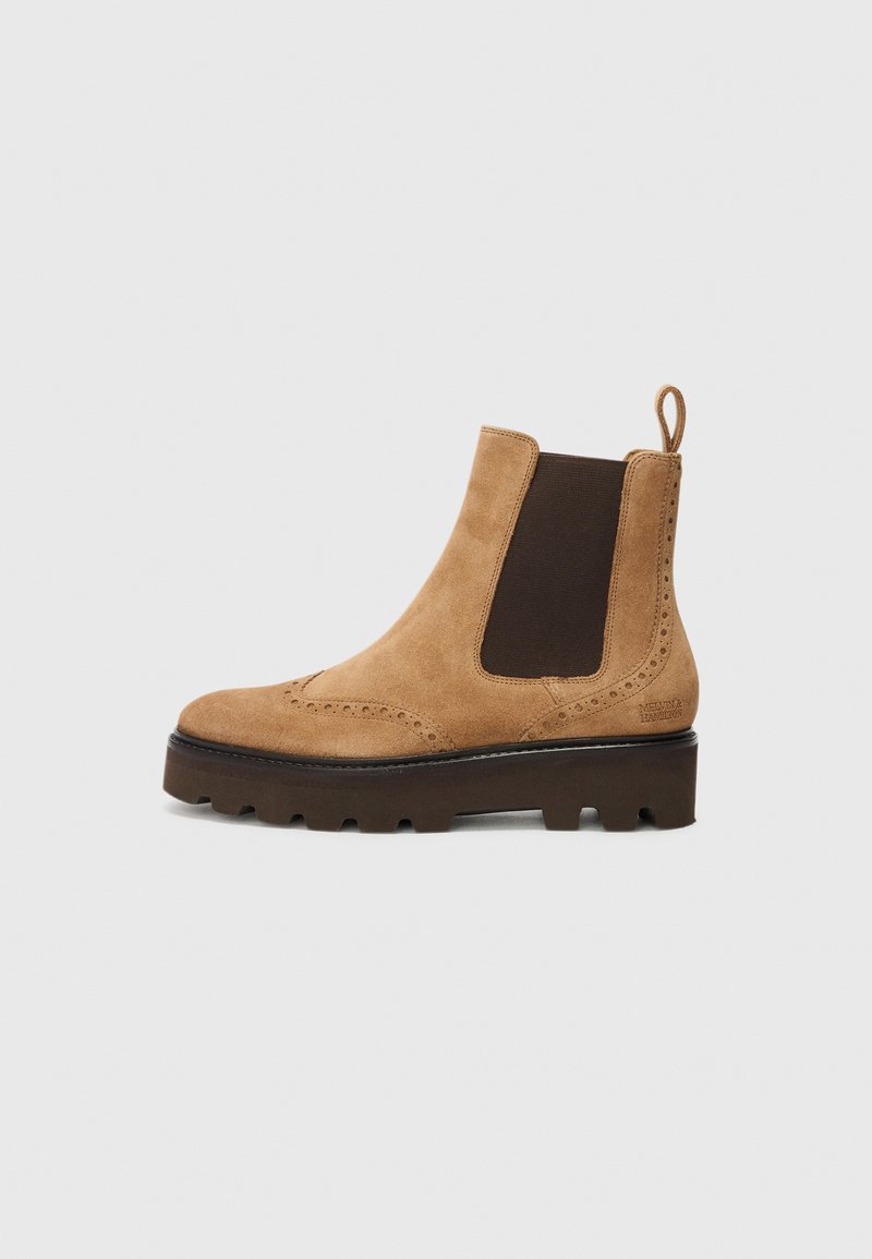 Bottines Chelsea en suede marron avec des panneaux latéraux élastiques, des détails en boutonnage, et une semelle en caoutchouc épaisse. Tirette à l'arrière pour une mise en chaussure facile.