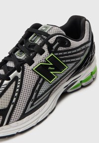 Chaussure de course grise et noire avec lacets noirs, accents vert citron vert et détail de semelle rembourrée sur un fond clair uni.