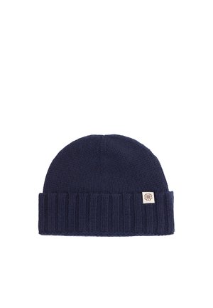 Marineblaue gerippte Strickmütze mit umgeschlagenem Bündchen und kleinem beigefarbenem Etikett mit symmetrischem Logo.