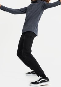 Blå mönstrad skjorta med slim fit, svarta byxor och svarta Vans-skor. Skjortan har små geometriska mönster och en ficka framtill.