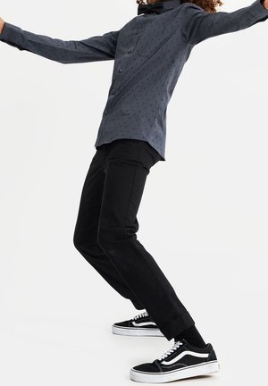 Blauwe gestreepte shirt met een slim fit, zwarte broek en zwarte Vans-schoenen. Het shirt heeft kleine geometrische ontwerpen en een voorkantzak.