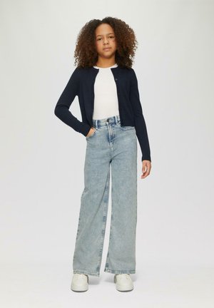 Granatowy kardigan, biały top, jasnoniebieskie dżinsy o szerokich nogawkach oraz białe trampki. Kardigan ma guziki, dżinsy są z wysokim stanem i prostym krojem.